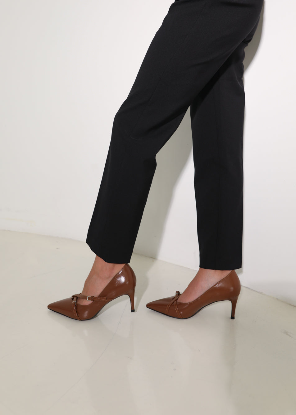 Person wearing black pants and brown high-heeled shoes on a white background