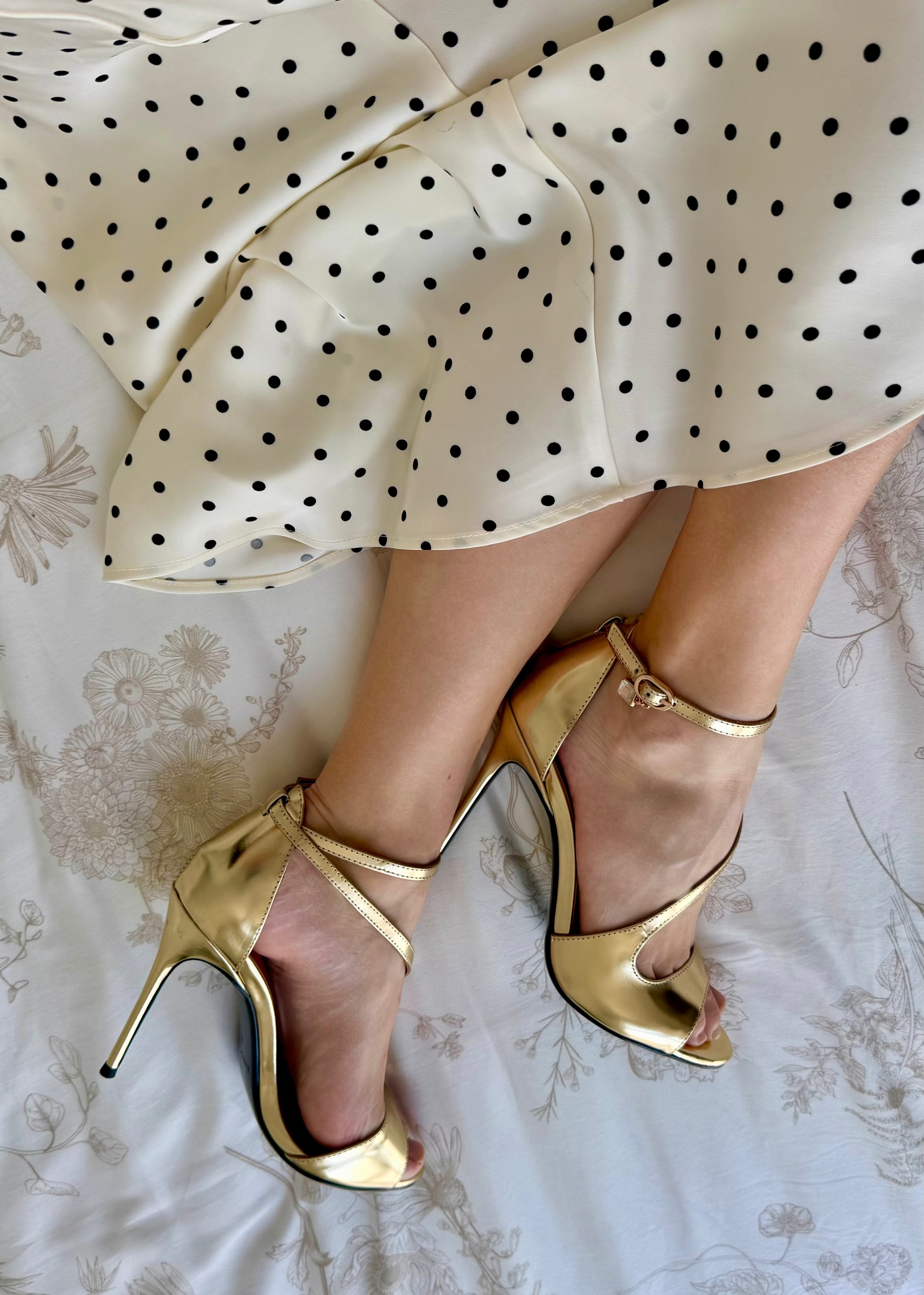 Gold high-heeled shoes worn with a polka dot skirt on a floral fabric background
