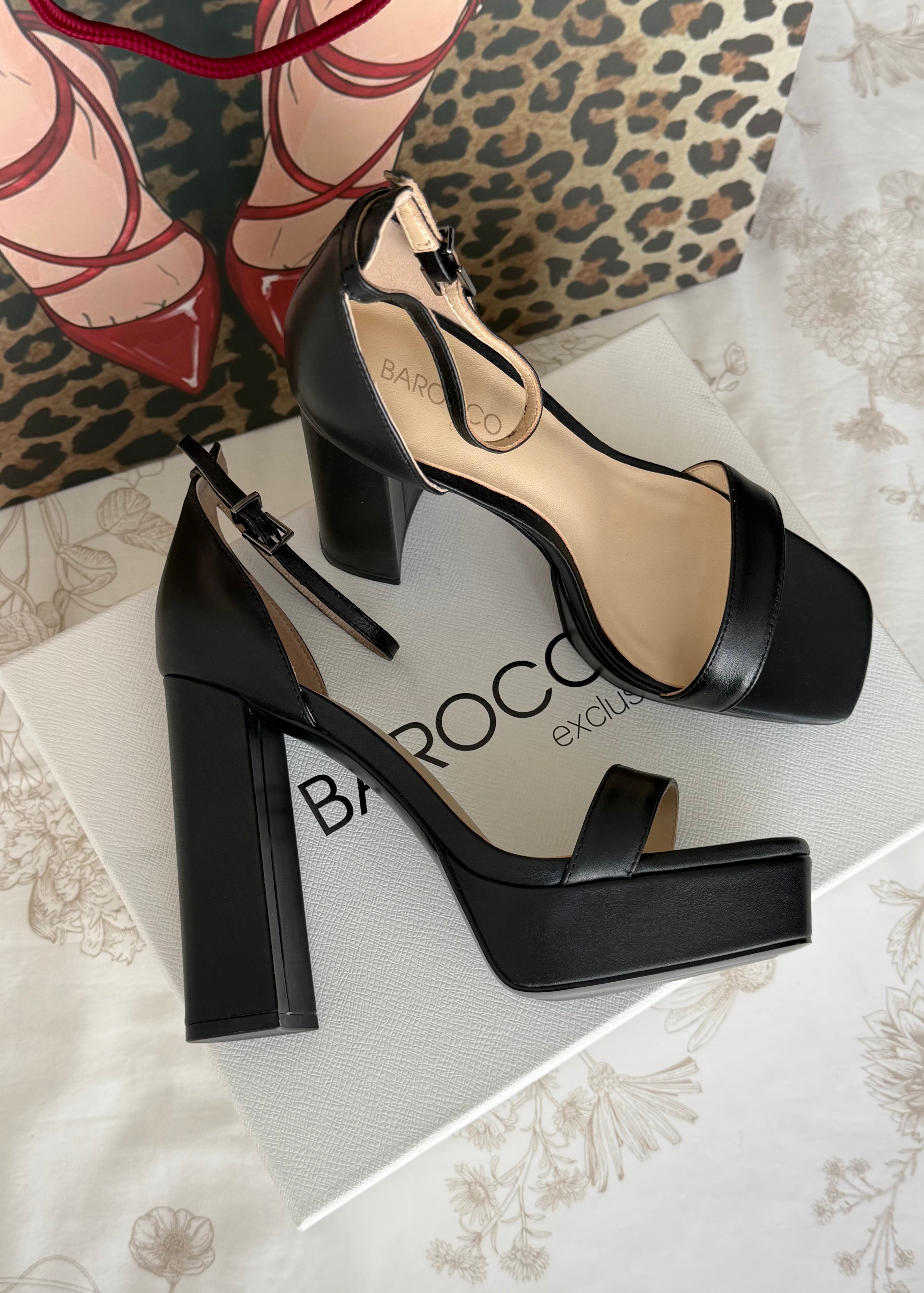Black high-heeled shoes on a light background with a leopard print bag.
