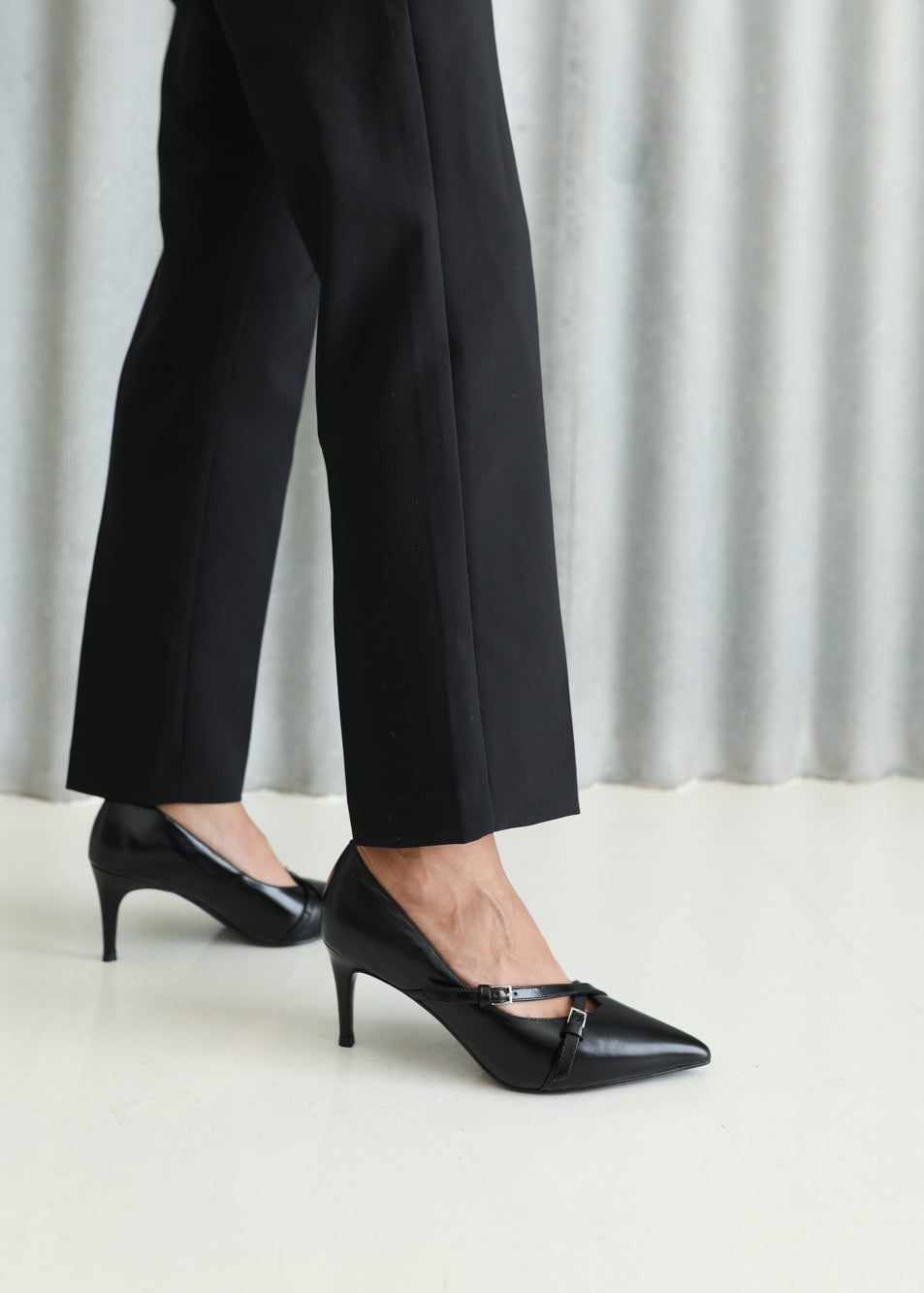 Person wearing black high-heeled shoes and black pants against a light background