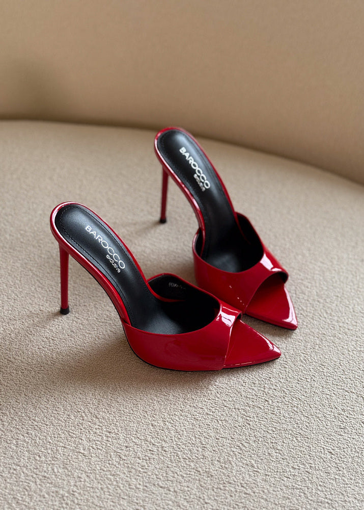 Red high-heeled shoes with a brand logo on a beige surface