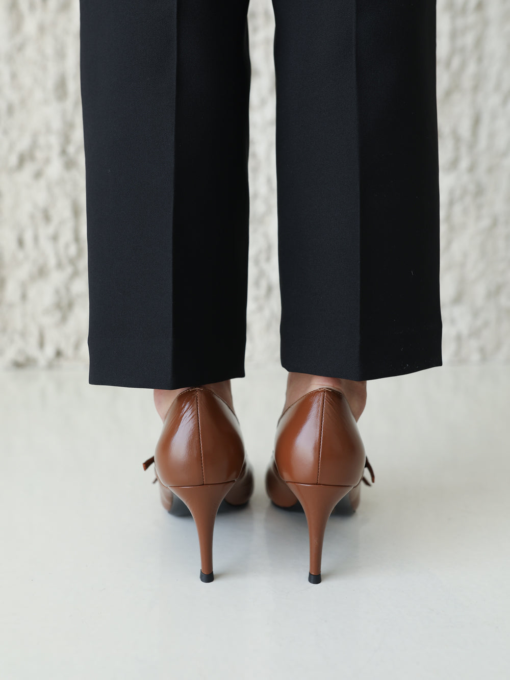 Brown high-heeled shoes worn with black pants against a light background