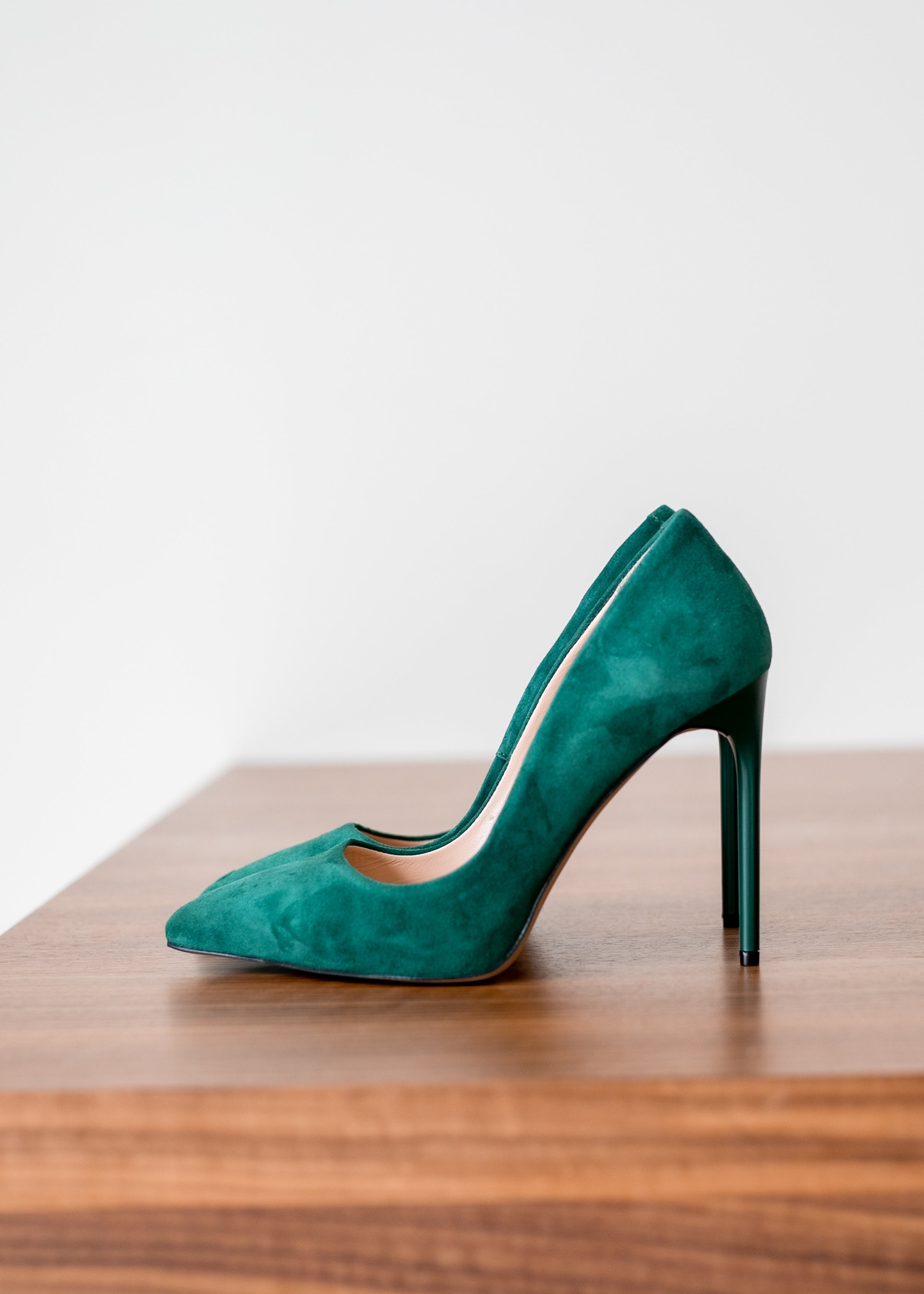 Emerald green suede stiletto heels on wooden surface, elegant pointed toe design