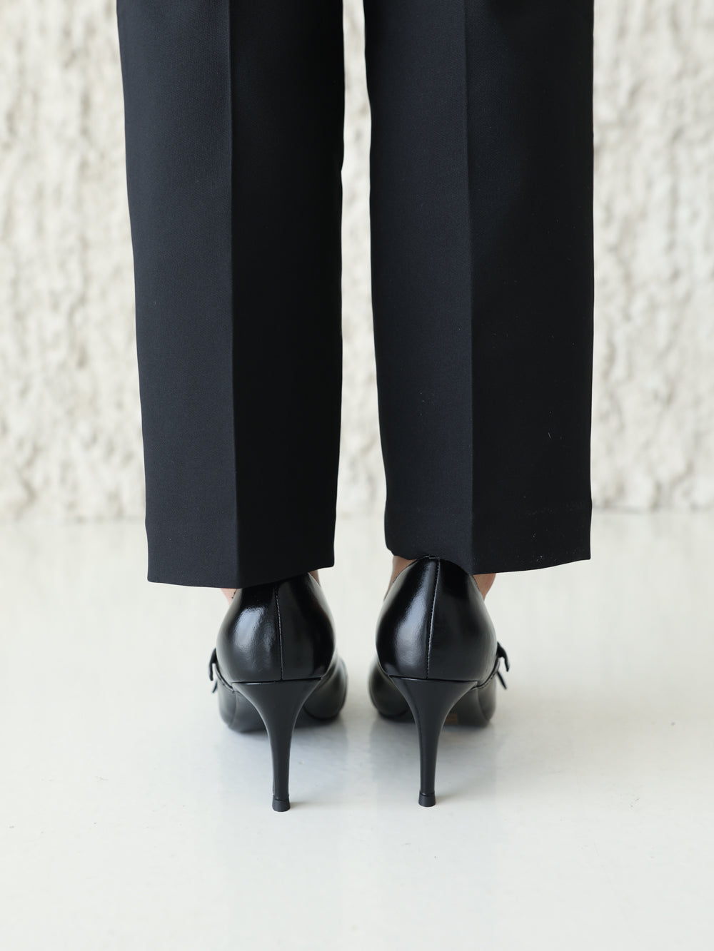 Black high-heeled shoes and black pants on a light background