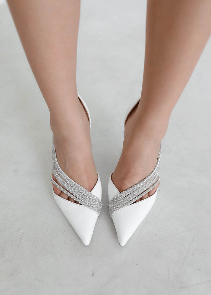 White high-heeled shoes with silver straps on a light gray background